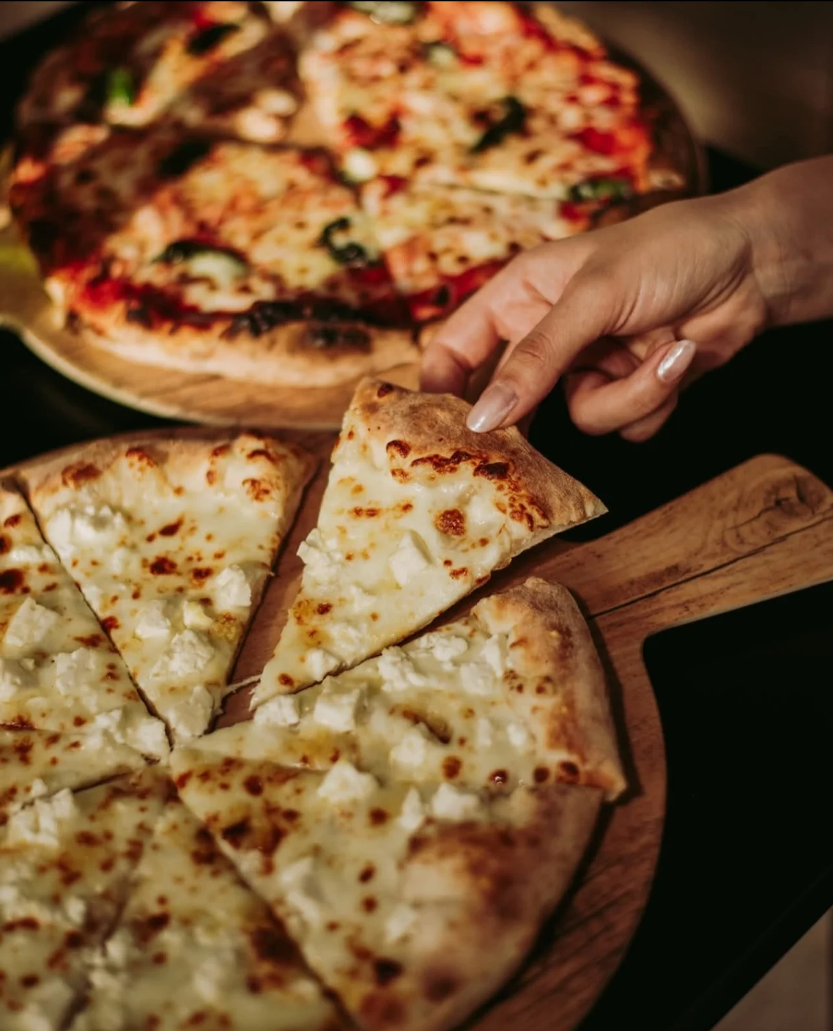 Fresh Neapolitan pizza on a light wooden table inside FOODURO pizzeria with wood-fired oven glowing in the background
